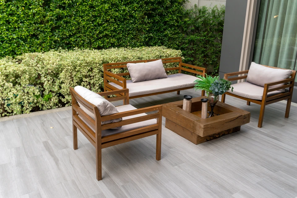 Terrasse extérieure aménagée avec salon de jardin en bois teck comprenant canapé deux places, deux fauteuils assortis avec coussins beiges, table basse carrée massive