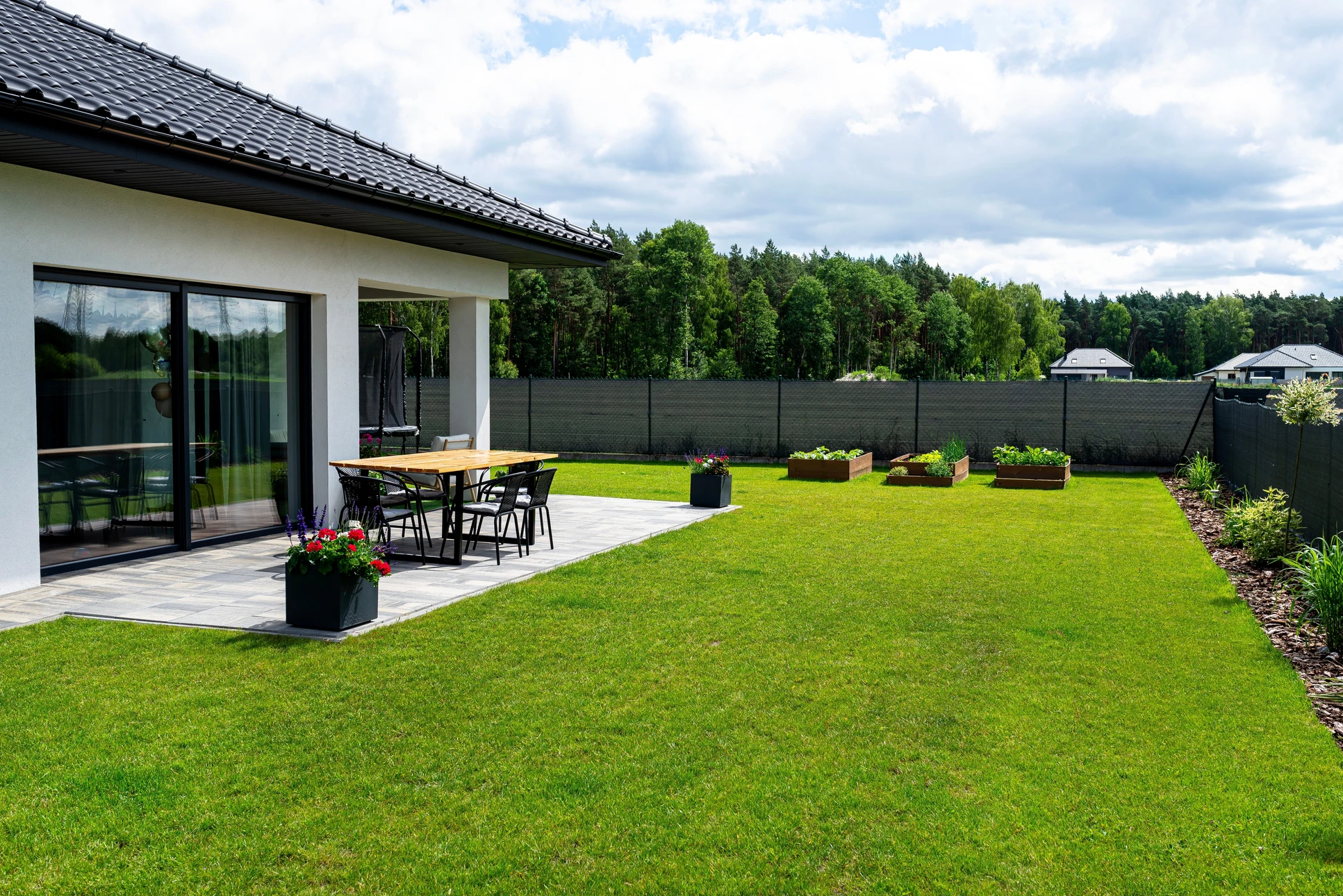 Homme en vêtements décontractés poussant une tondeuse à gazon thermique sur pelouse verte bien entretenue dans jardin résidentiel ensoleillé avec arbres en arrière-plan