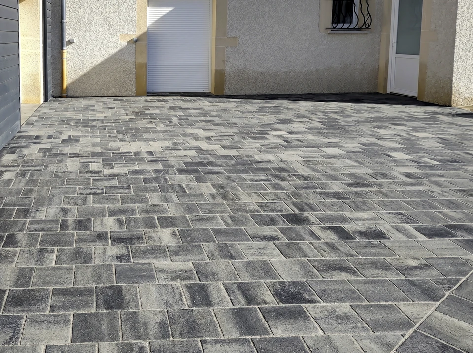 Ouvrier en tenue de sécurité orange posant des pavés gris sur chantier extérieur
