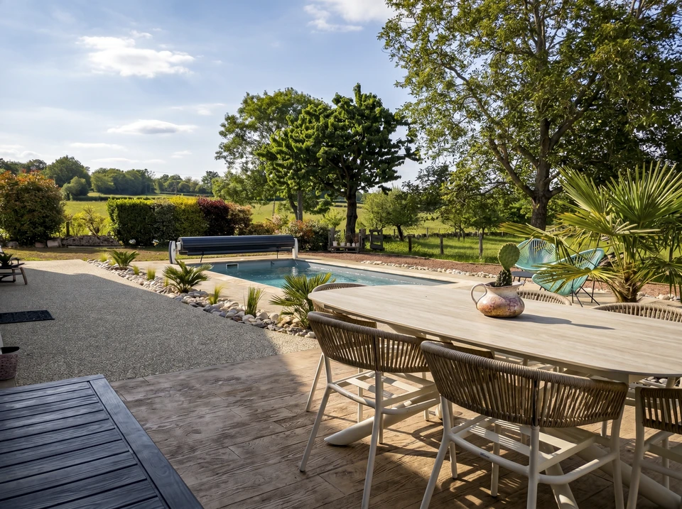 Jardin paysager avec terrasse en bois surélevée, mobilier de jardin en fer forgé noir et coussins beiges